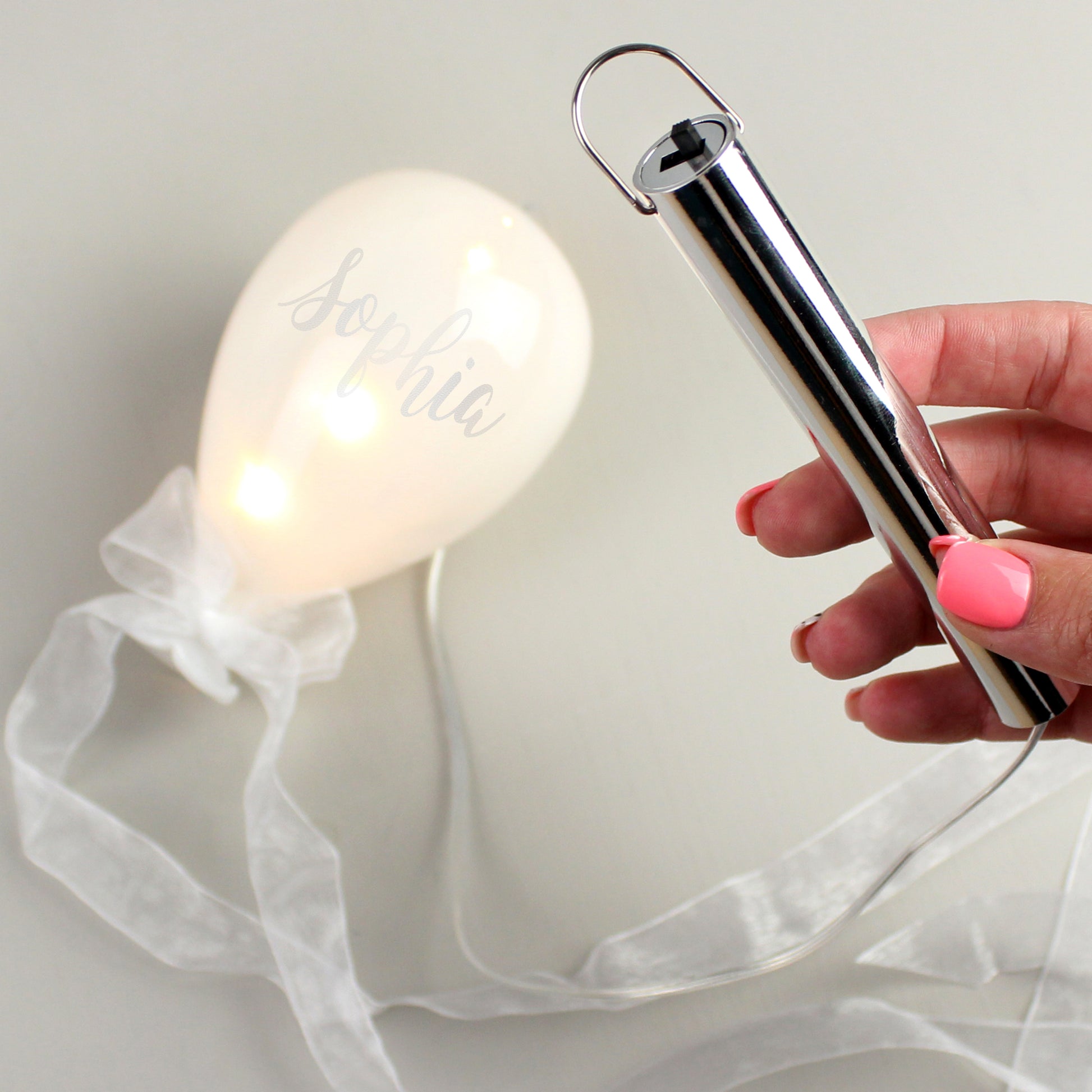 Hand holding a small lamp with a white ribbon against a light background