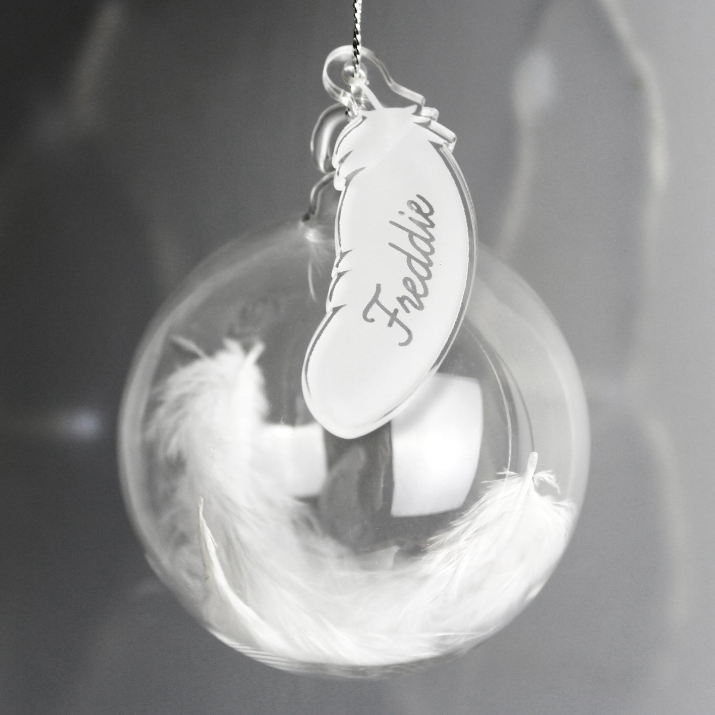 Decorative sphere with feathers and a feather-shaped tag engraved with 'Freddie' on a dark background.