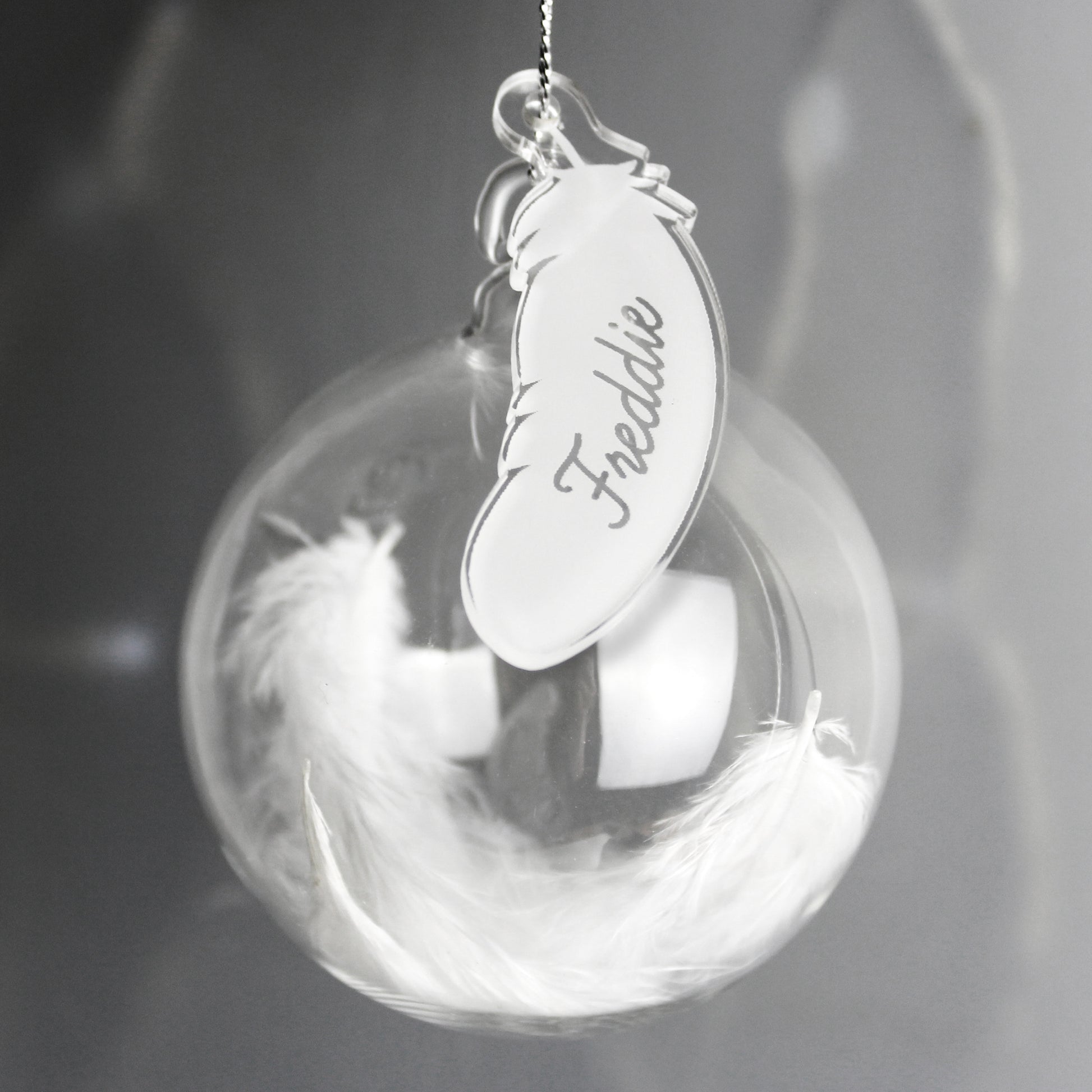 Decorative sphere with feathers and a feather-shaped tag engraved with 'Freddie' on a dark background.