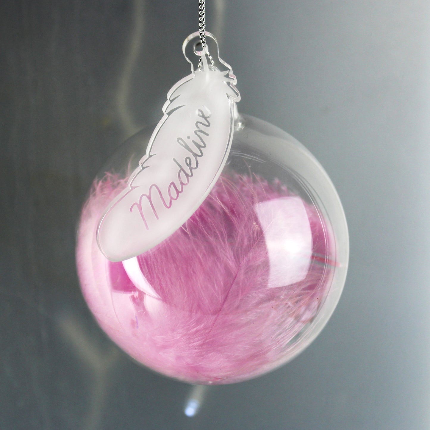 Clear sphere with pink feather and 'Madelin' tag on a gray background