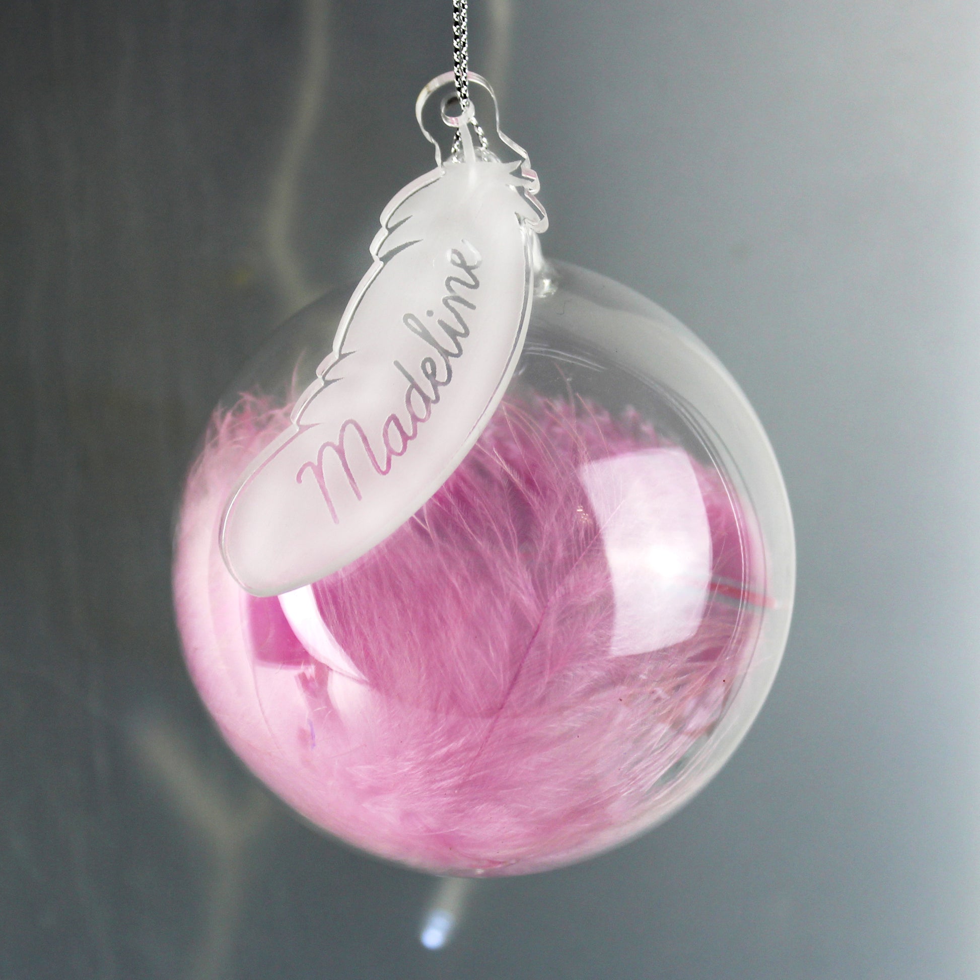 Clear sphere with pink feather and 'Madelin' tag on a gray background