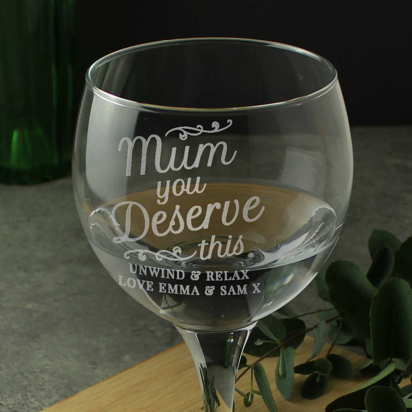 Wine glass with engraved message on a wooden surface with greenery