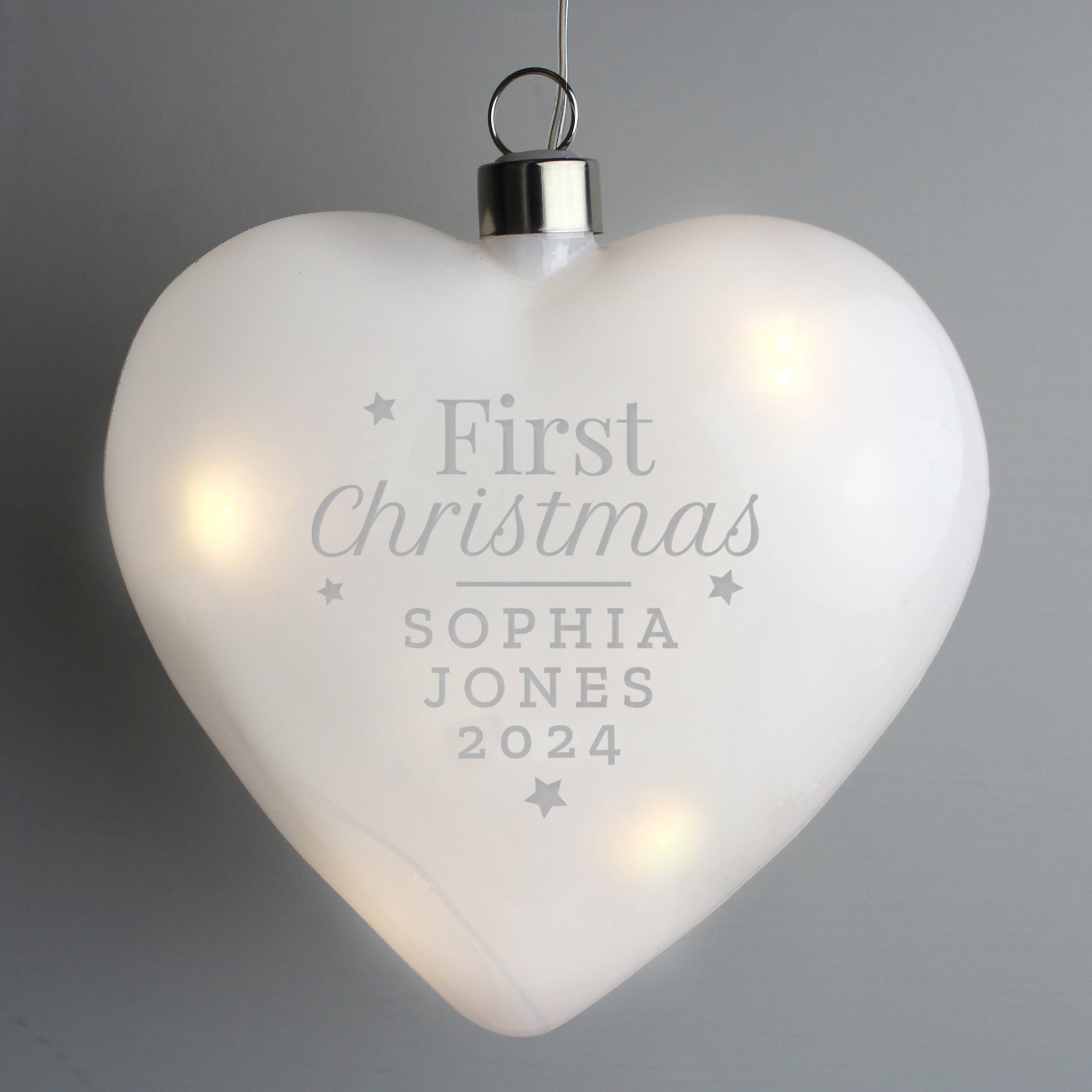 Heart-shaped ornament with 'First Christmas' engraving on a gray background