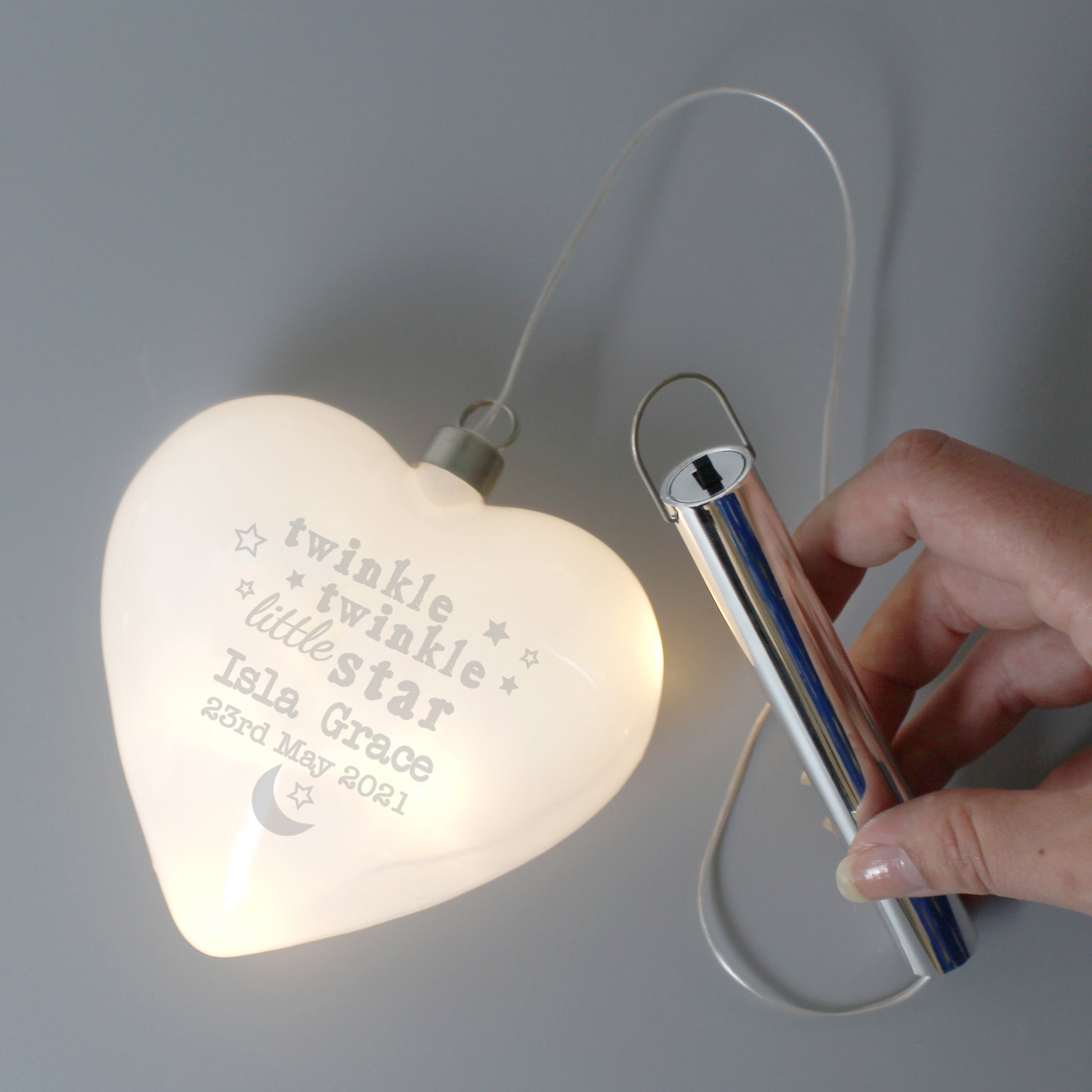 Heart-shaped light with engraved text held by a hand against a gray background