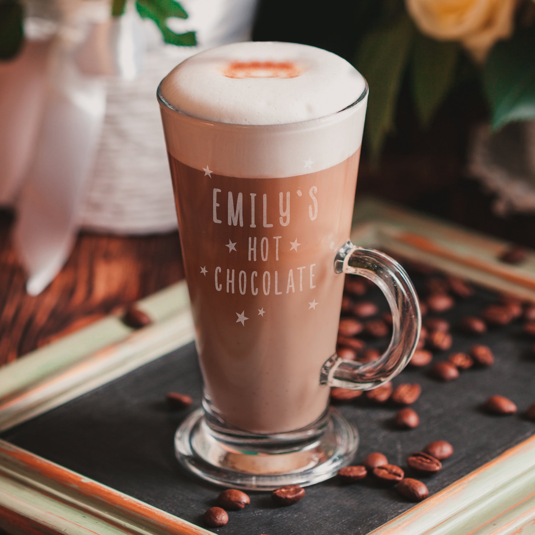 Glass of hot chocolate with 'EMILY'S HOT CHOCOLATE' text on a dark surface with coffee beans.