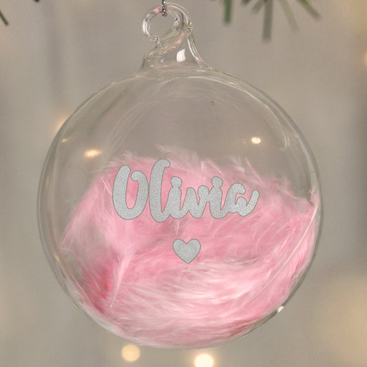 Personalised Clear glass ornament with pink feathers and 'Olivia' text on a blurred background