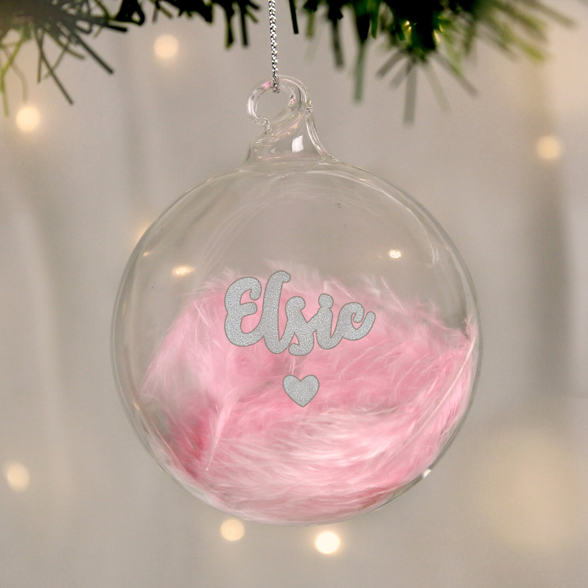 Clear Christmas ornament with pink feather filling and 'Elsie' text, hanging on a tree.