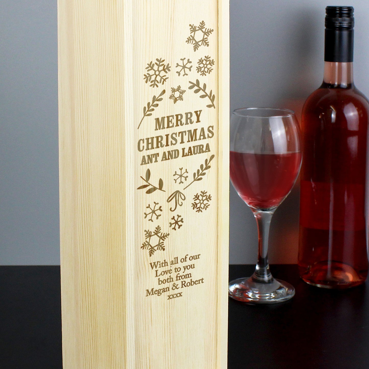 Wooden wine box with engraved text, next to a bottle of red wine and a glass.