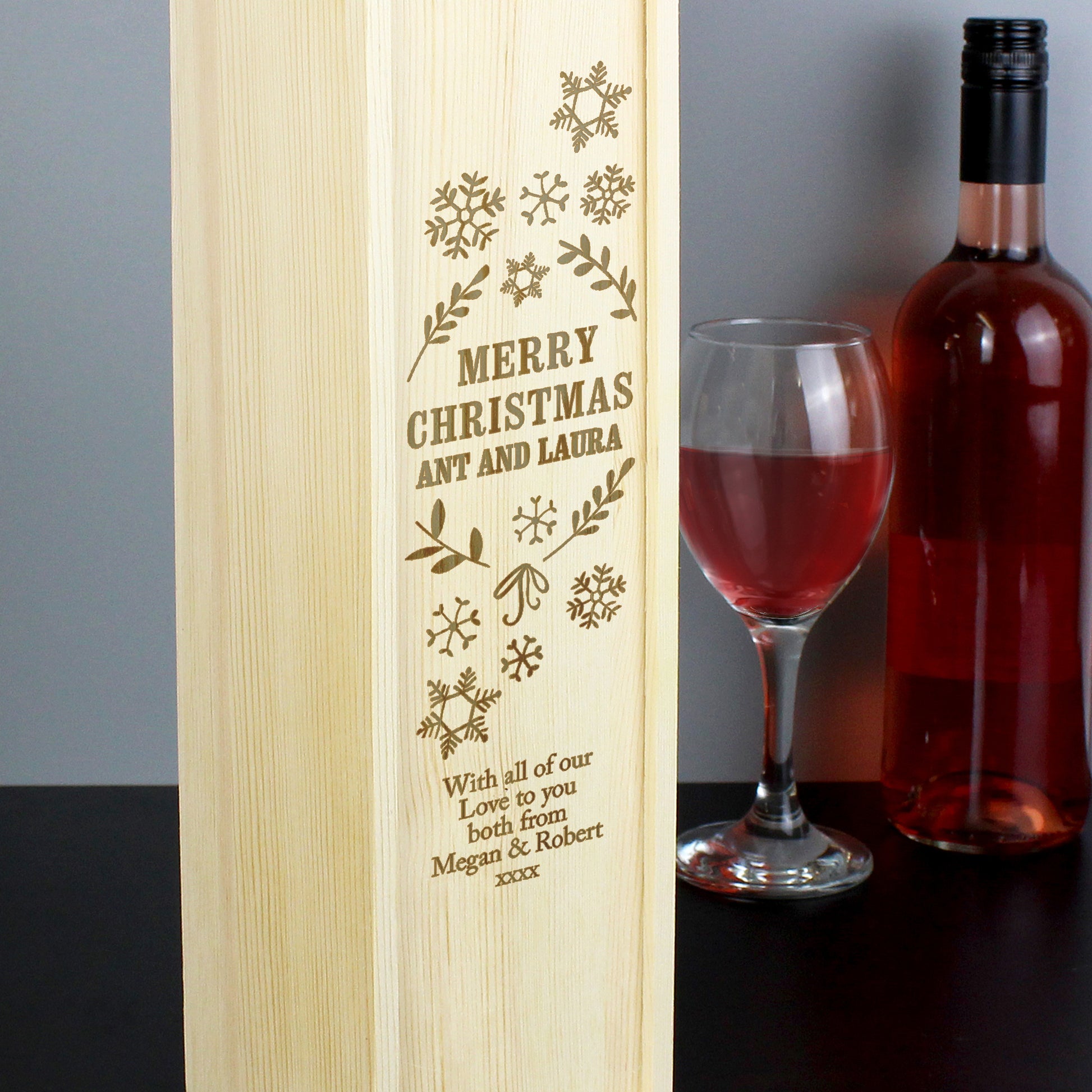 Wooden wine box with engraved text, next to a bottle of red wine and a glass.