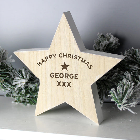 Personalised Wooden star ornament with 'Happy Christmas George XXX' engraving, surrounded by festive greenery.