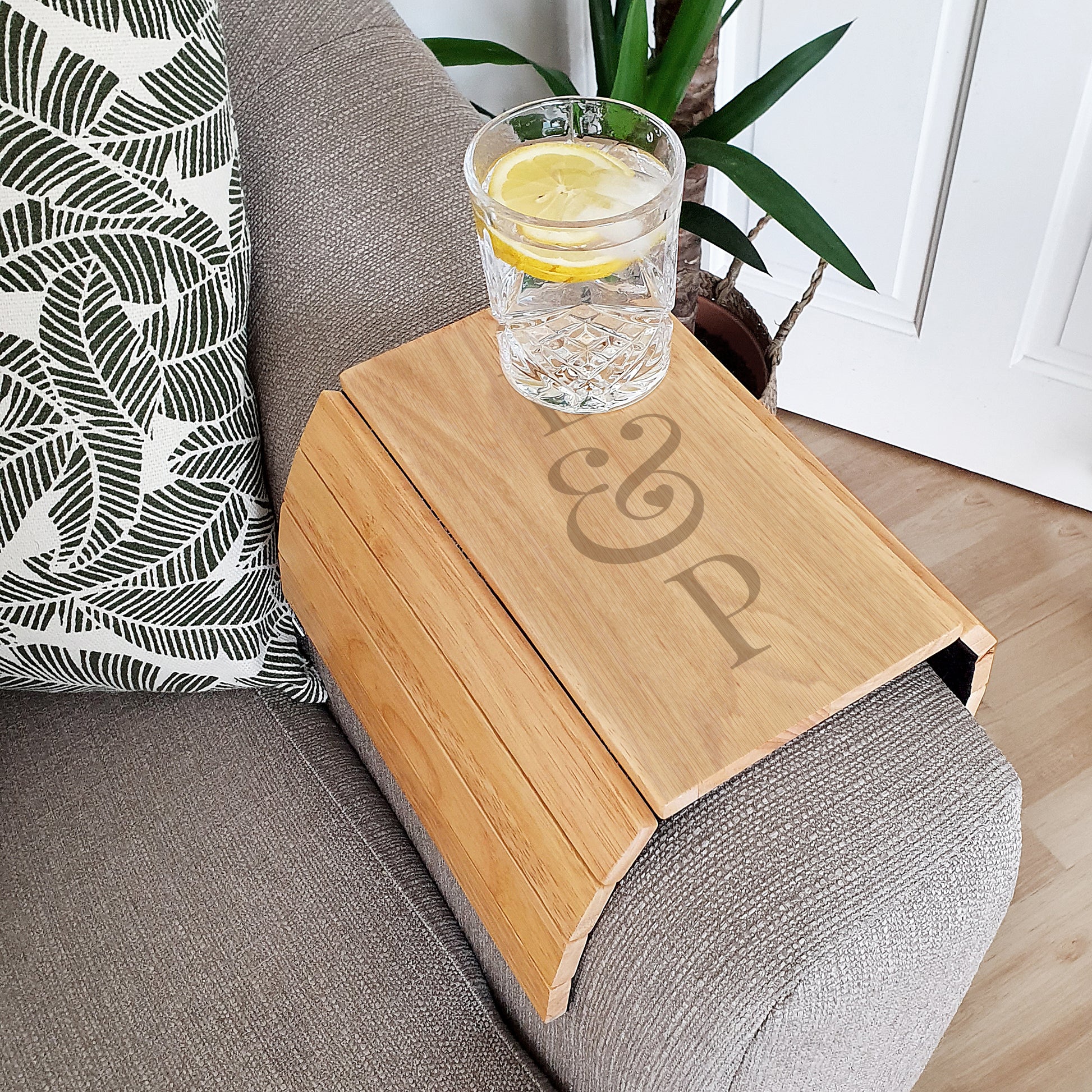 Wooden tray with initials on a couch holding a glass of water with lemon slices.