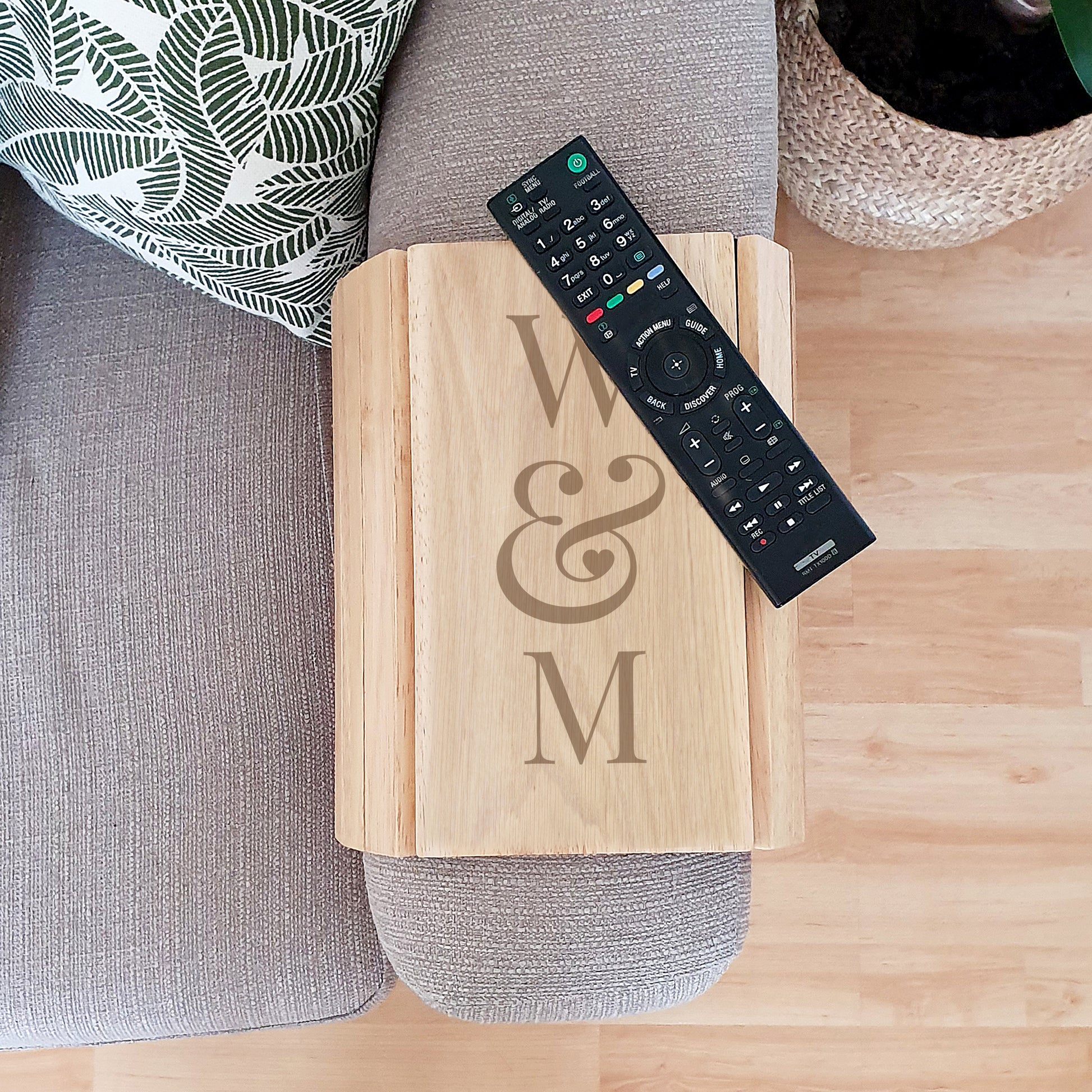 Wooden tray with 'W & M' engraving on a wooden surface with a remote control.