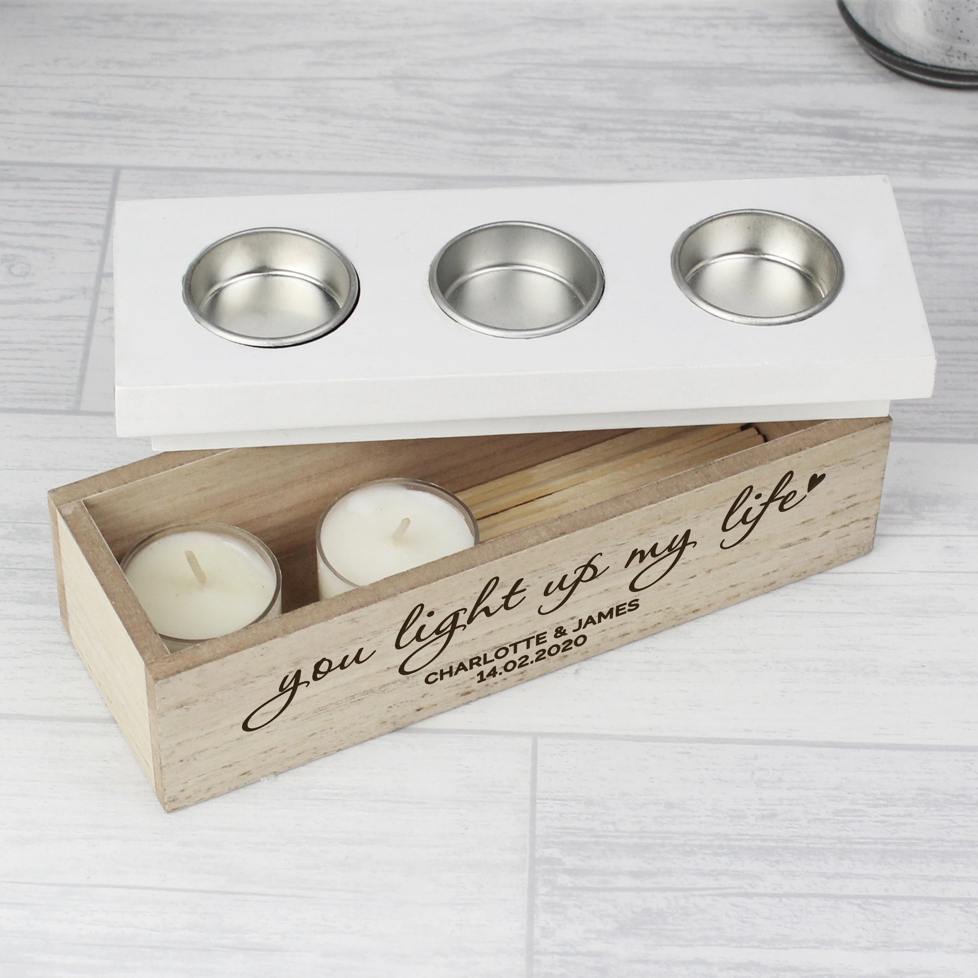 Wooden candle holder with three candles and engraved message on a light wooden surface