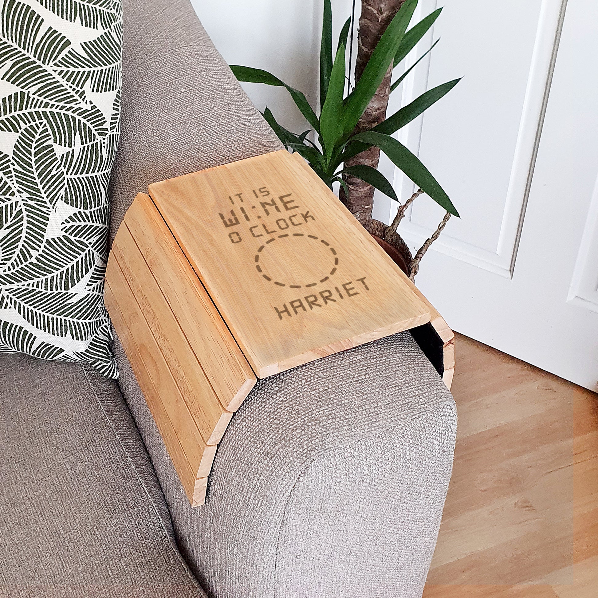 Wooden sofa tray on a grey sofa with a plant in the background
