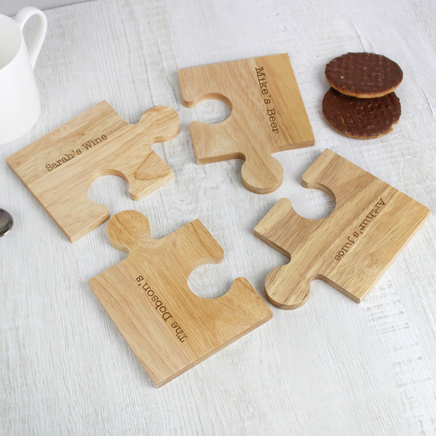 Four wooden puzzle piece coasters with personalised engraved names on a white surface.