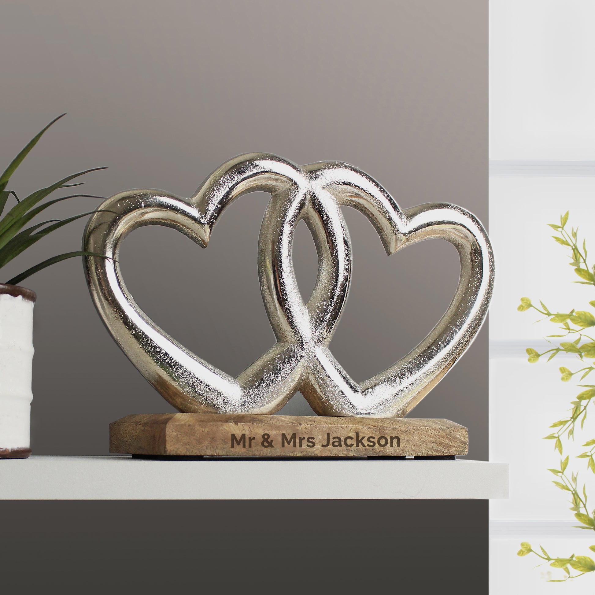Decorative sculpture of two interlocking hearts on a wooden base with 'Mr & Mrs Jackson' engraving, against a neutral background.