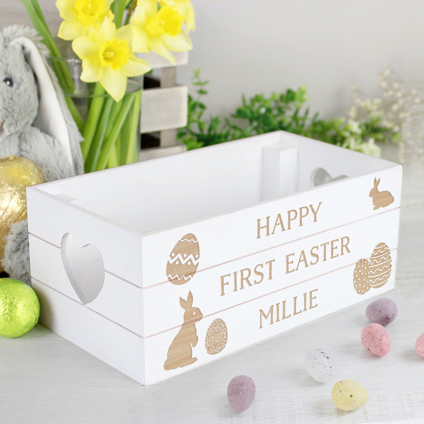 White Easter-themed wooden crate with 'Happy First Easter Millie' text, surrounded by Easter decorations.