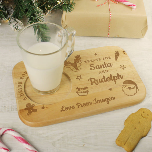 Wooden tray with engraved text, glass of milk, and gingerbread cookie on a festive background.