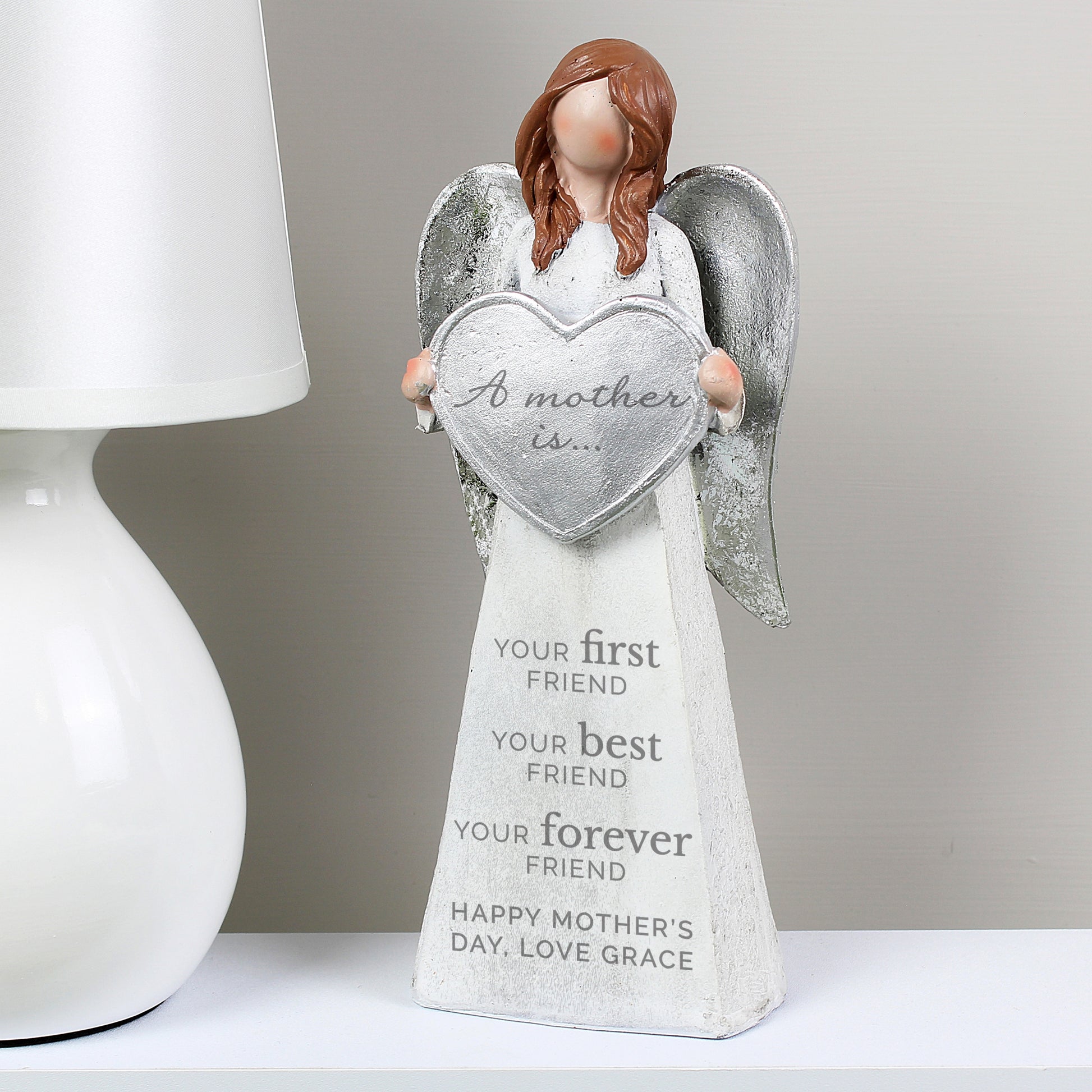 Decorative angel figurine holding a heart-shaped plaque with text on a white surface.