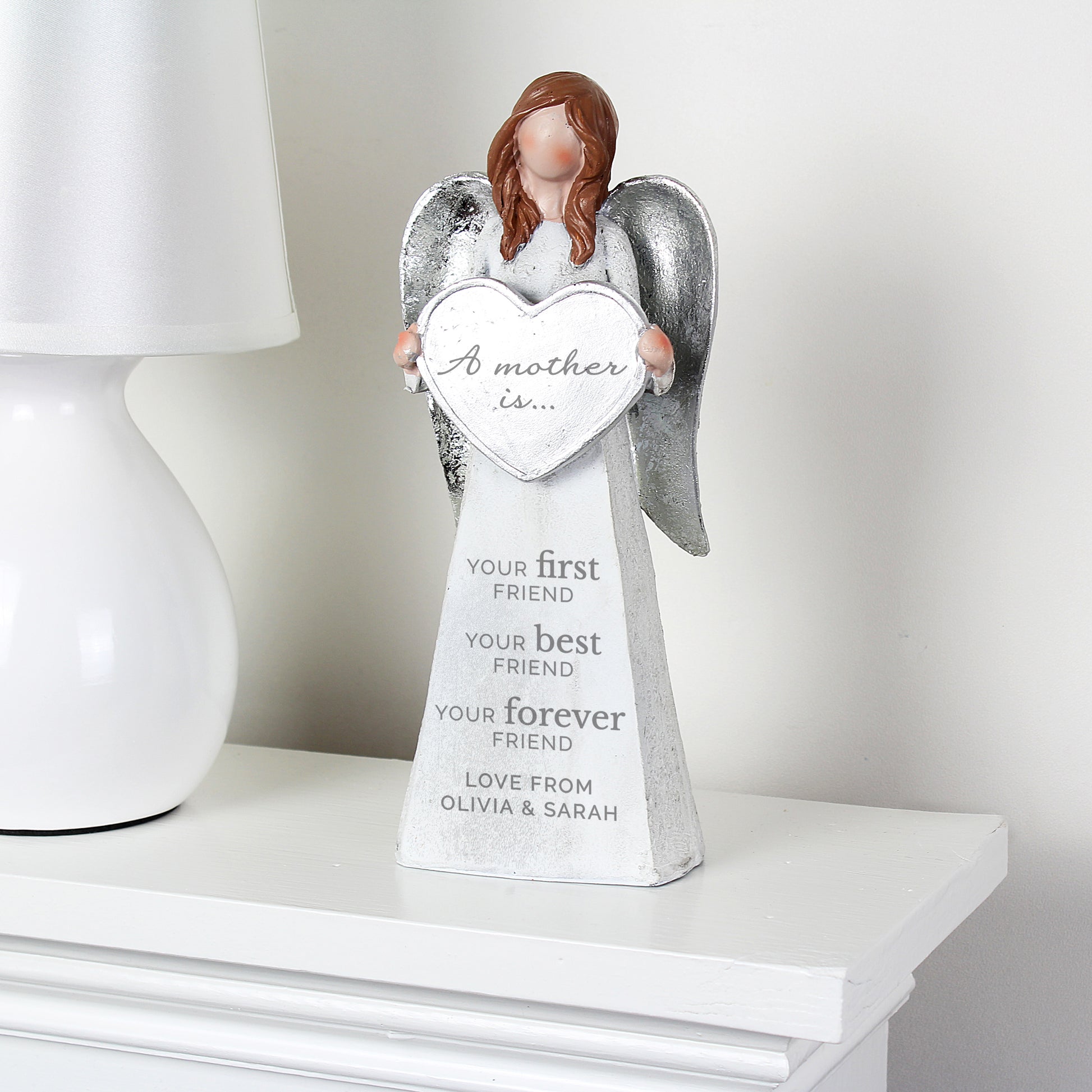Decorative angel figurine holding a heart with engraved text on a white surface.