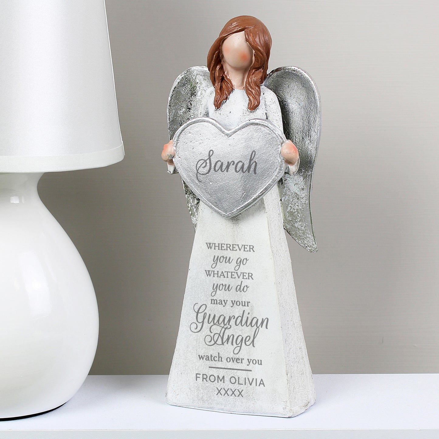Angel figurine holding a heart-shaped plaque with engraved text on a white surface.