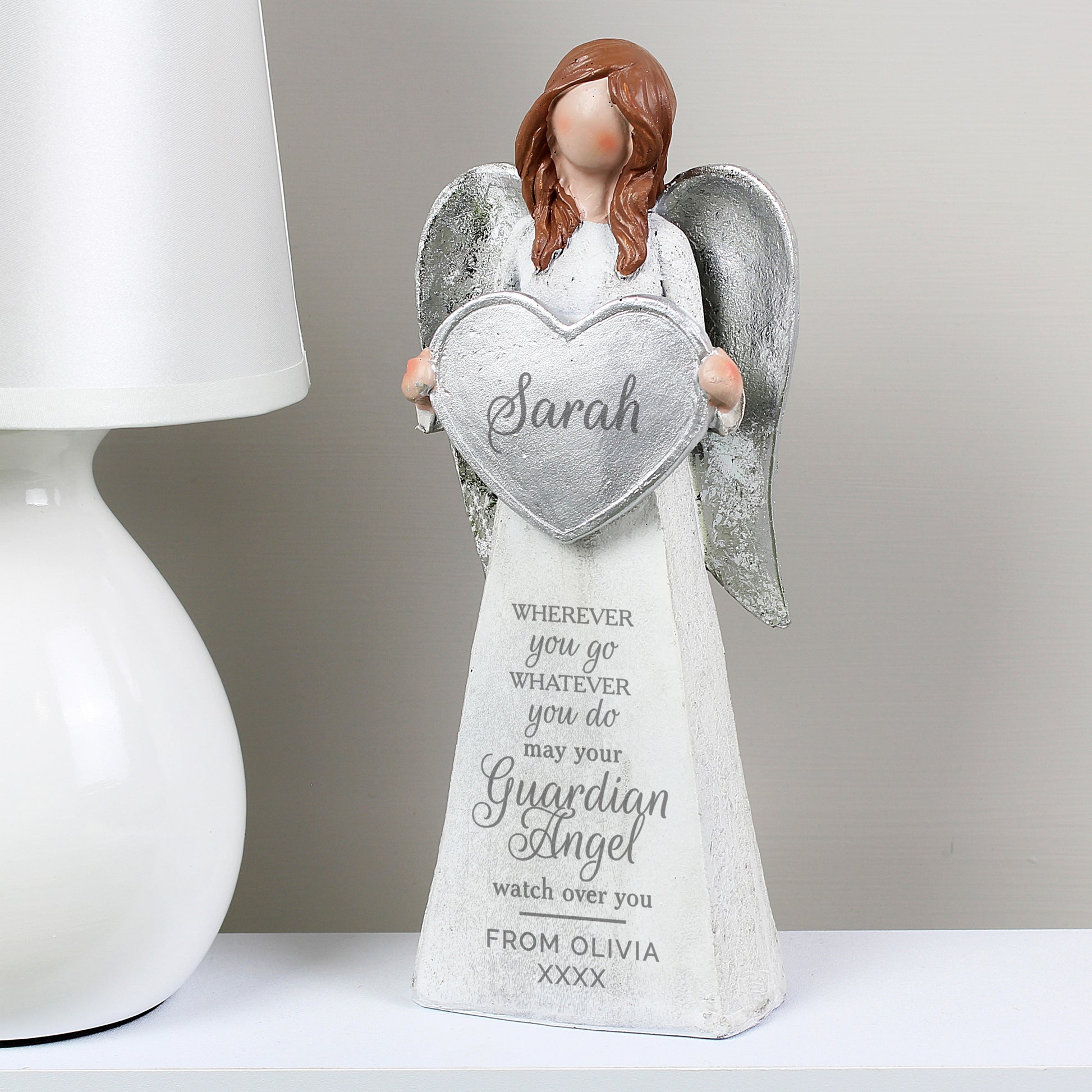Angel figurine holding a heart-shaped plaque with engraved text on a white surface.