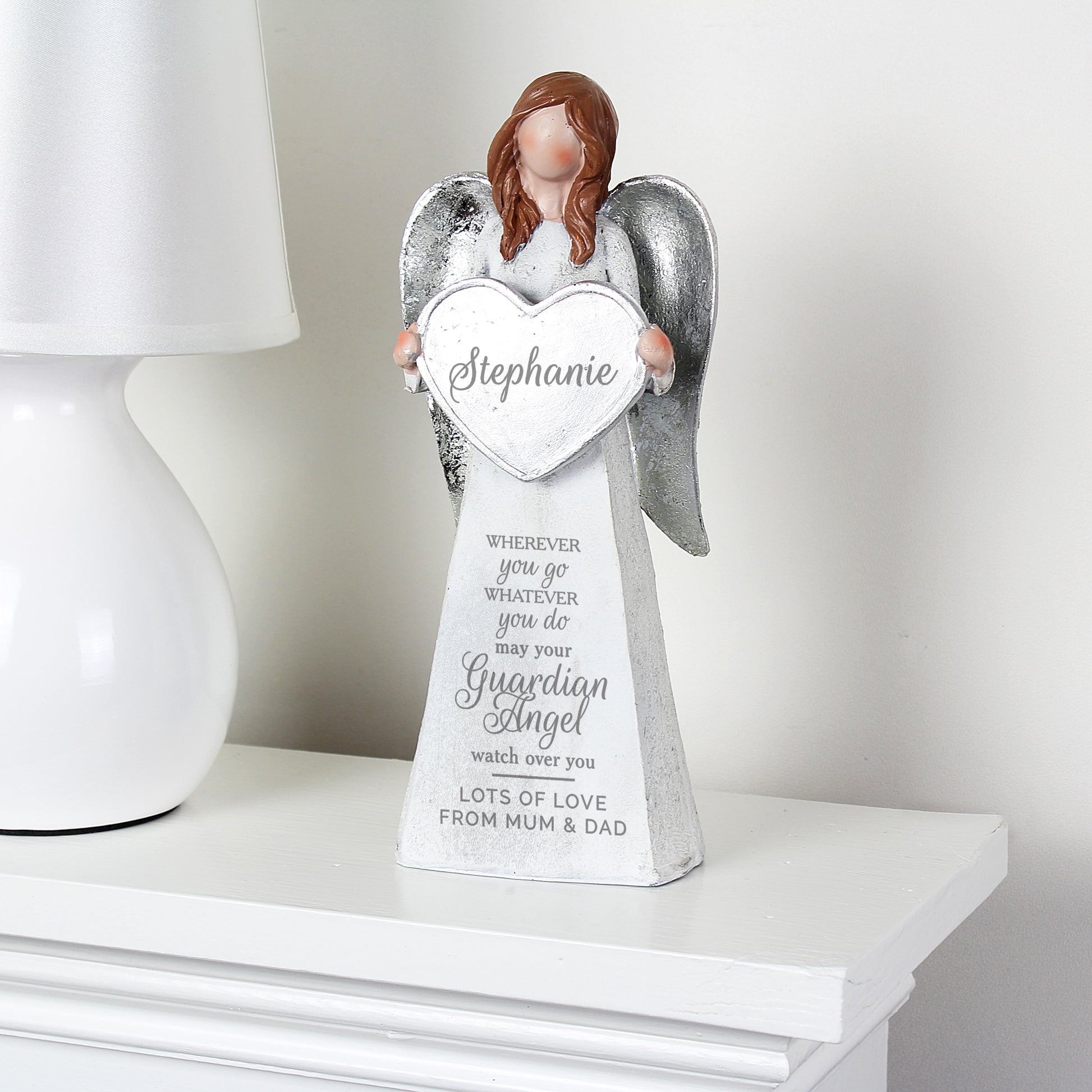 Decorative angel figurine holding a heart-shaped sign with engraved text on a white surface.