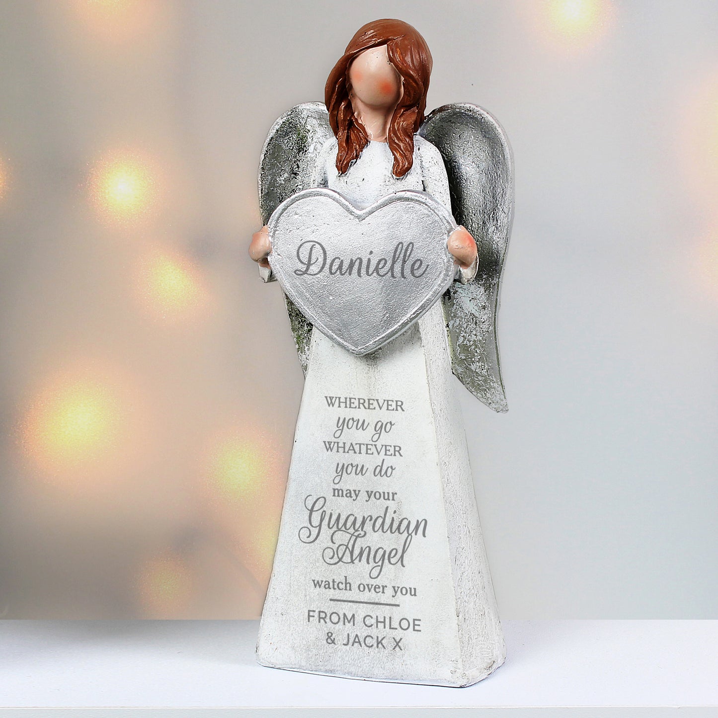 Angel figurine holding a heart-shaped sign with engraved text on a blurred light background