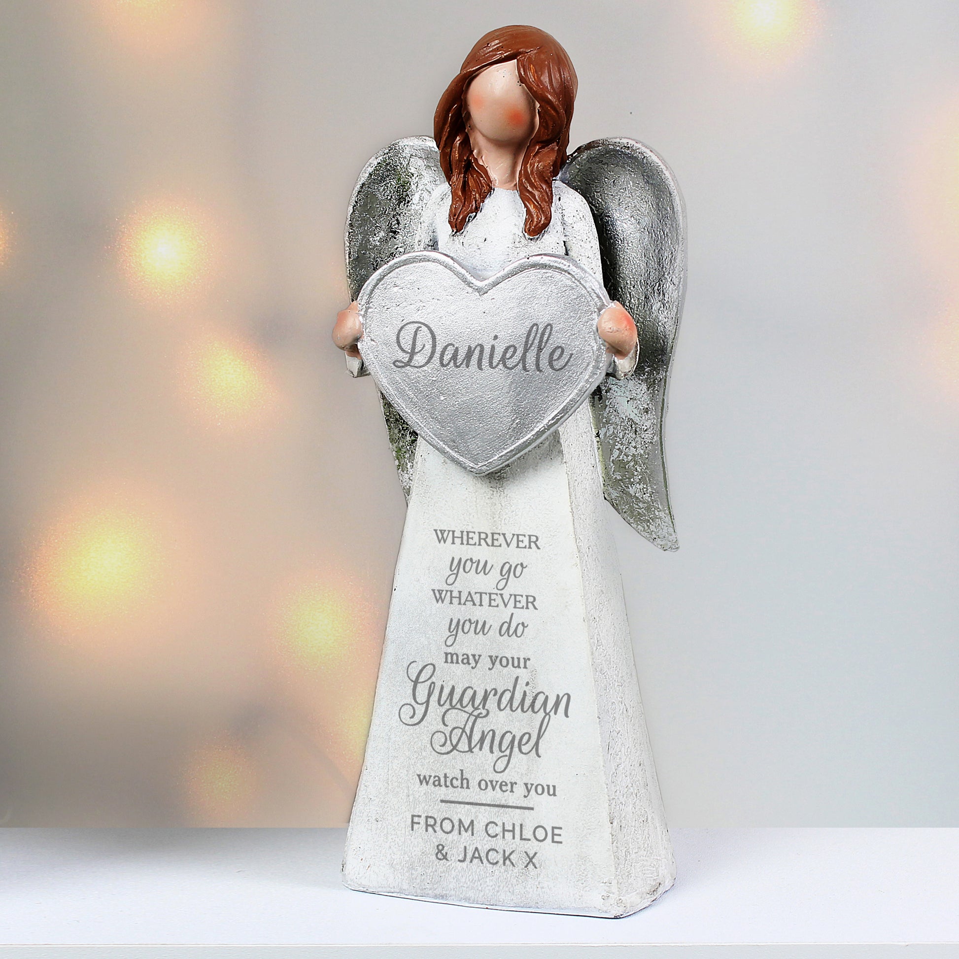 Angel figurine holding a heart-shaped sign with engraved text on a blurred light background