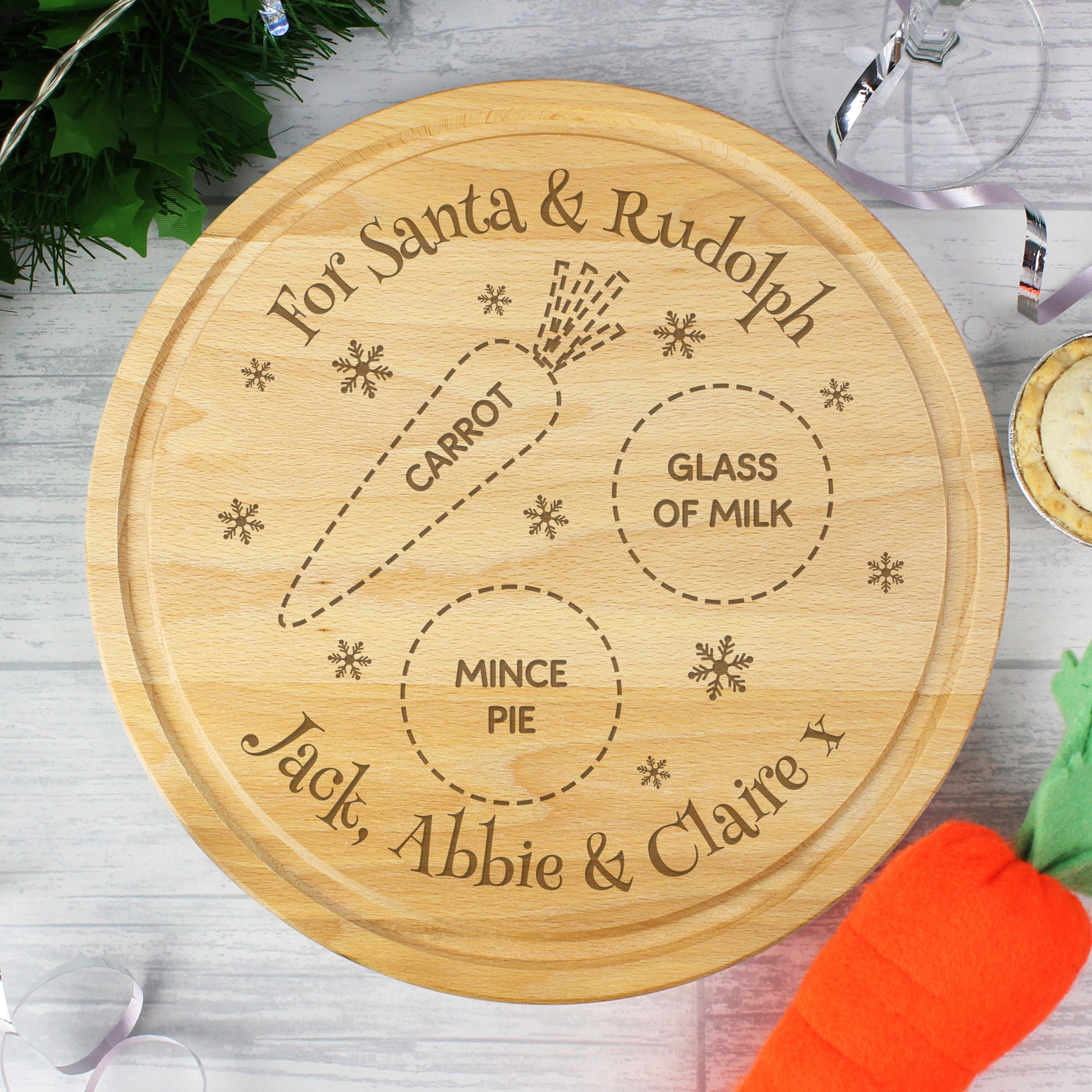 Wooden cutting board with engraved text for Santa and Rudolph, including a carrot, glass of milk, and mince pie, on a wooden surface.