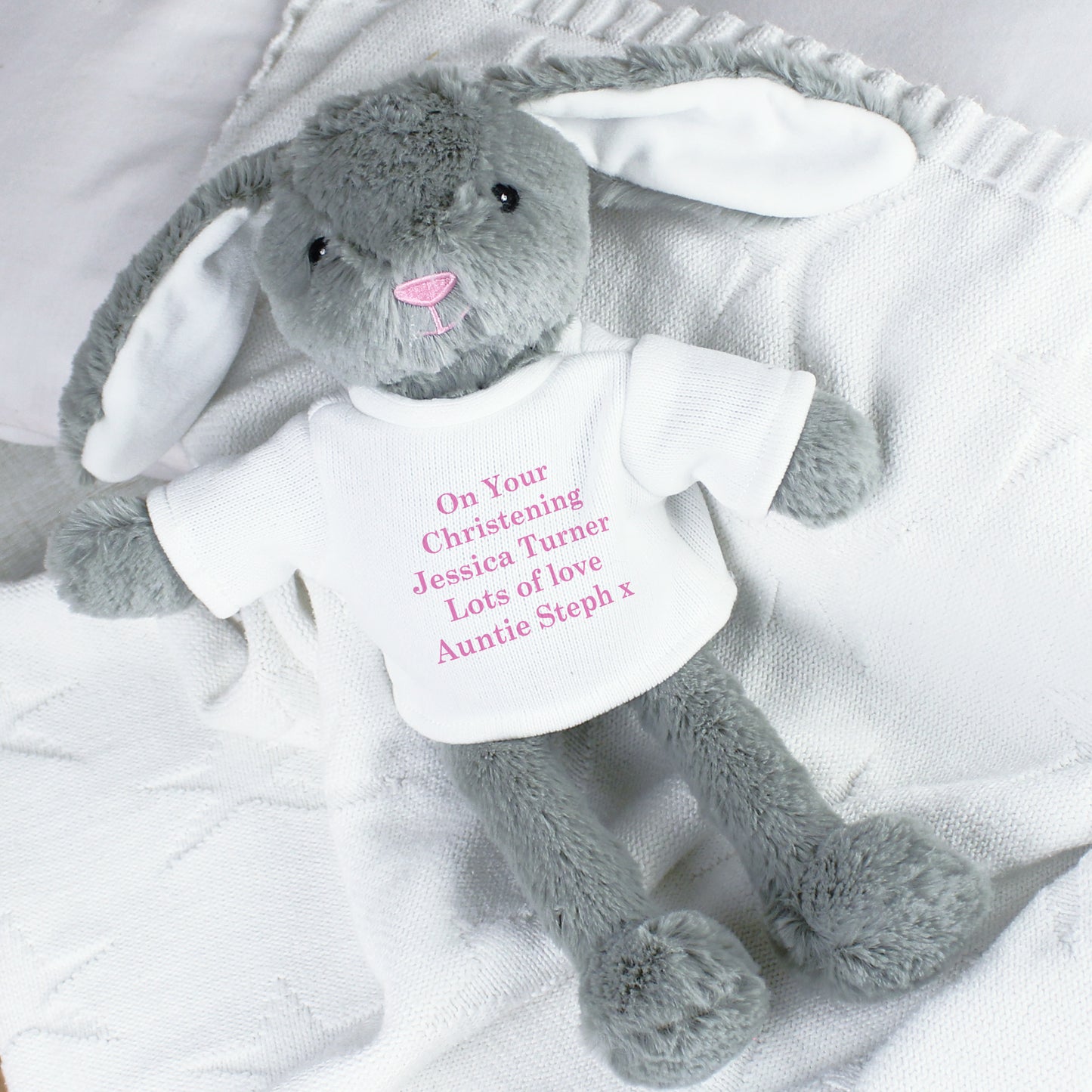Grey plush bunny with a white shirt on a white blanket