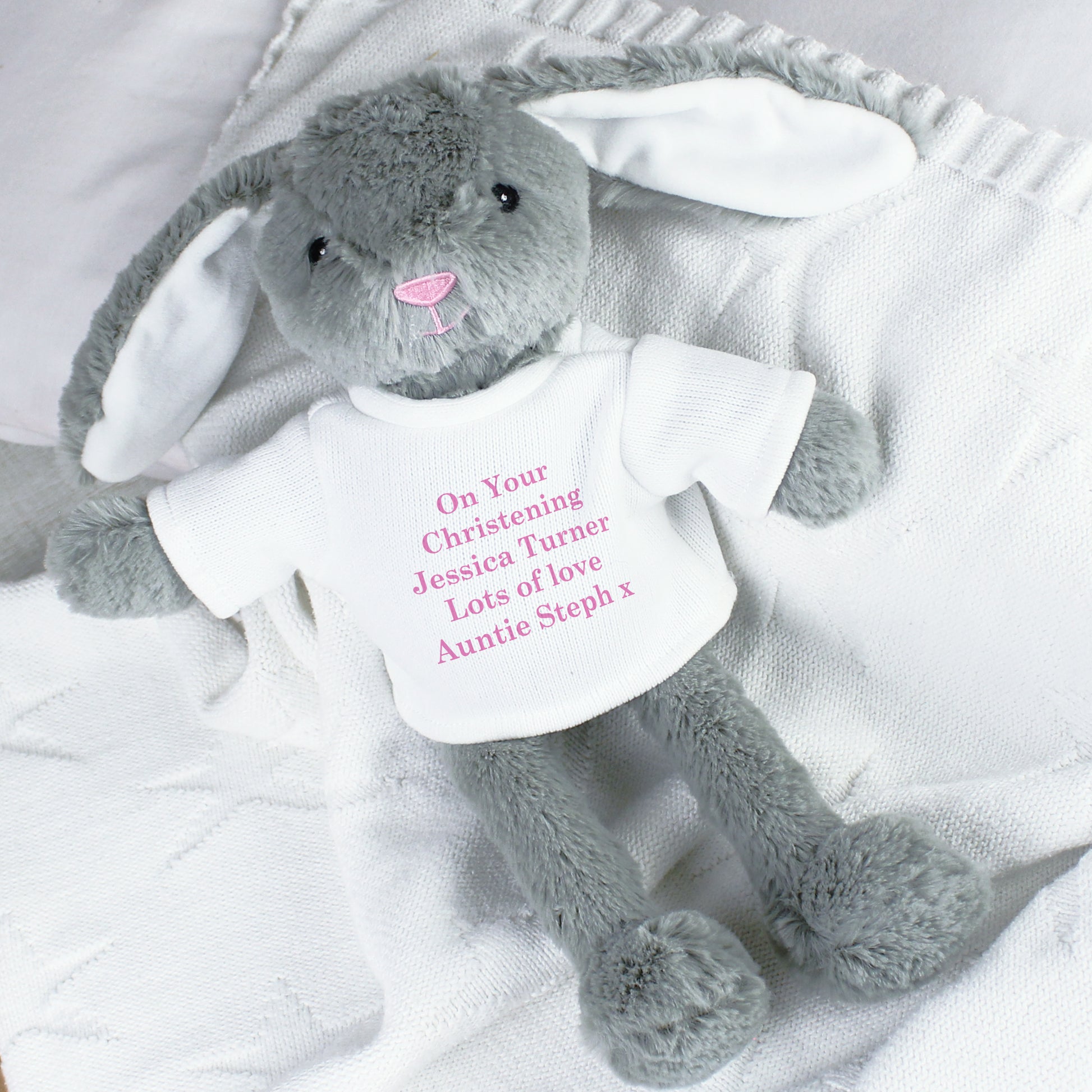 Grey plush bunny with a white shirt on a white blanket