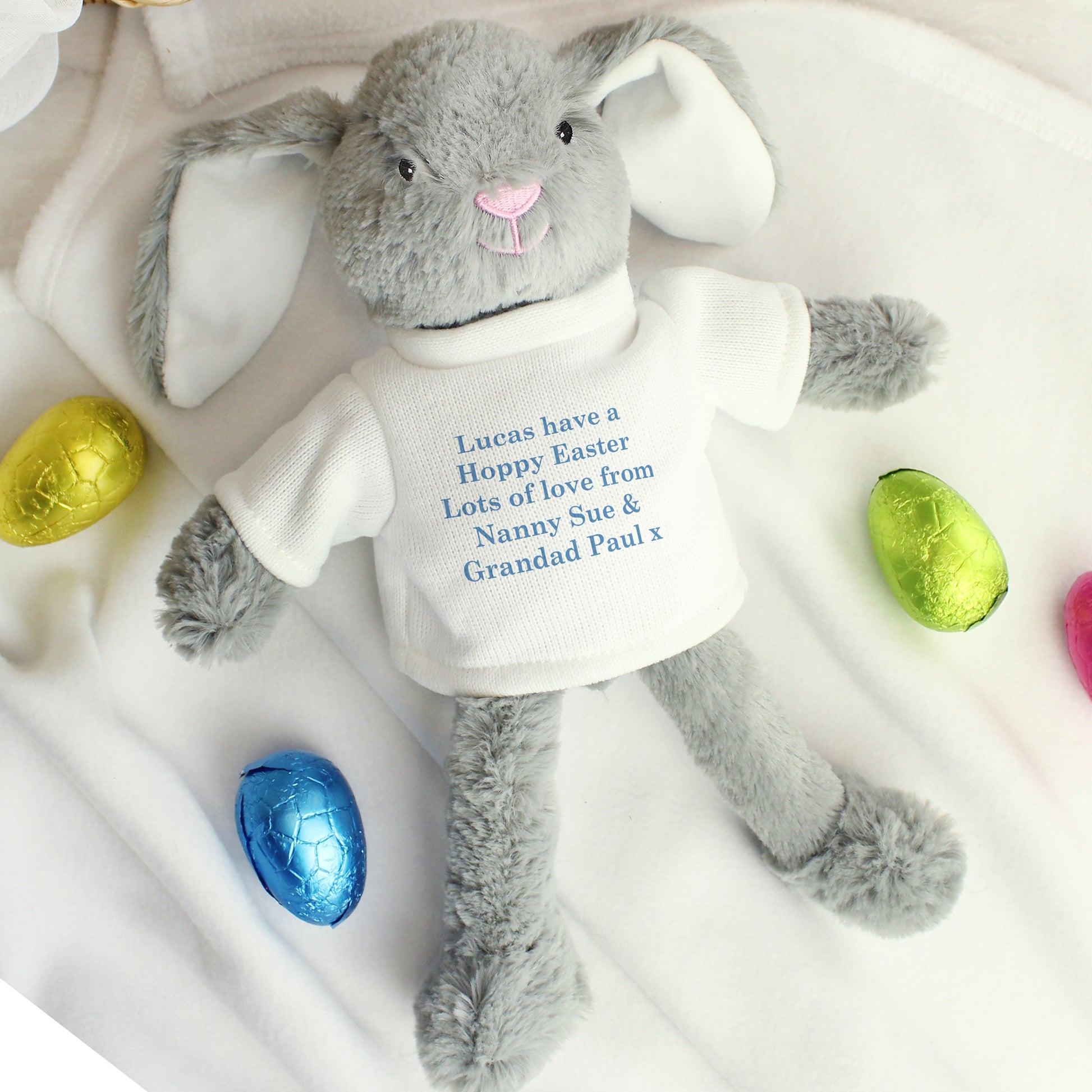 Grey plush bunny with a white shirt displaying a message, surrounded by colorful Easter eggs on a white background.