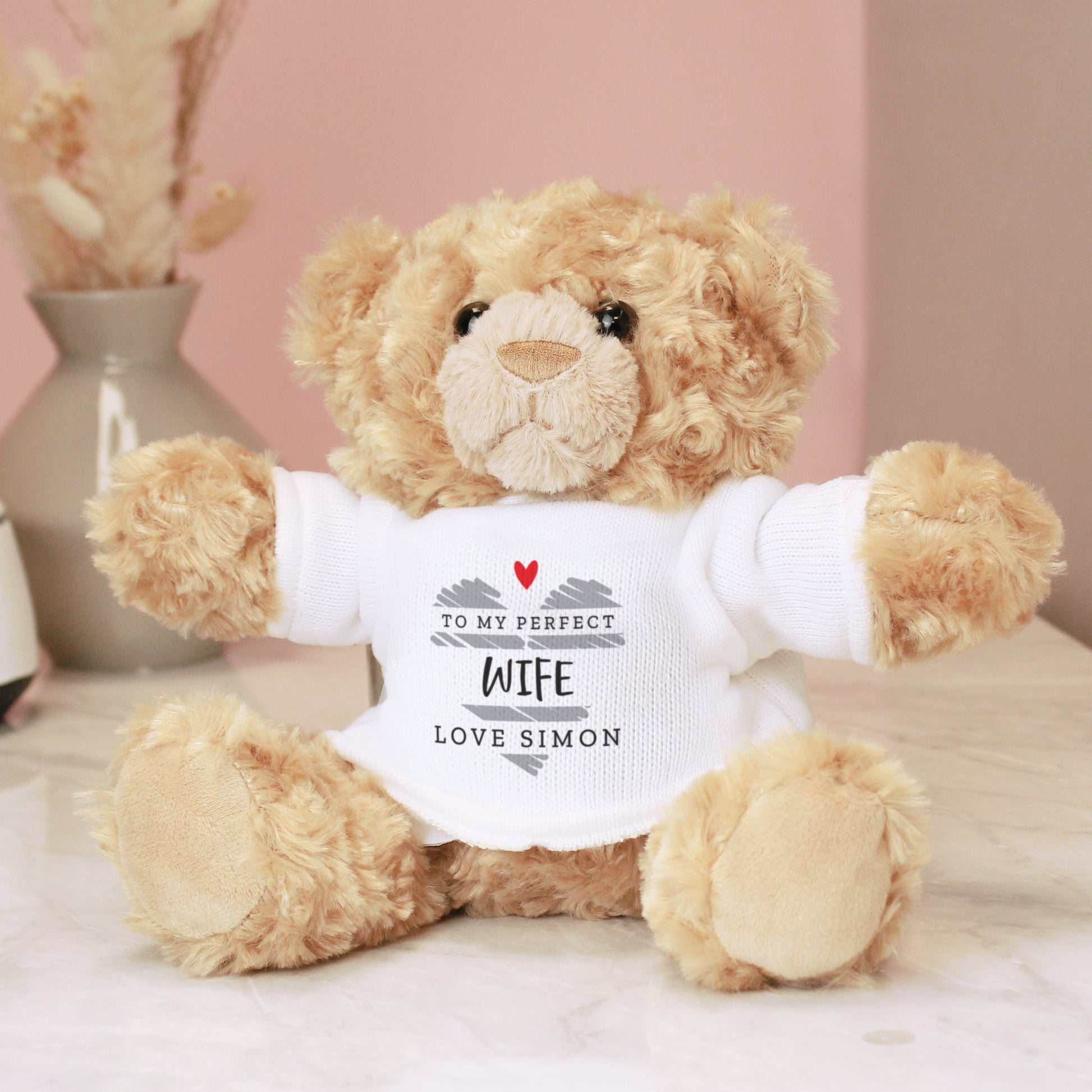 Teddy bear wearing a white shirt with personalized text on a soft pink background