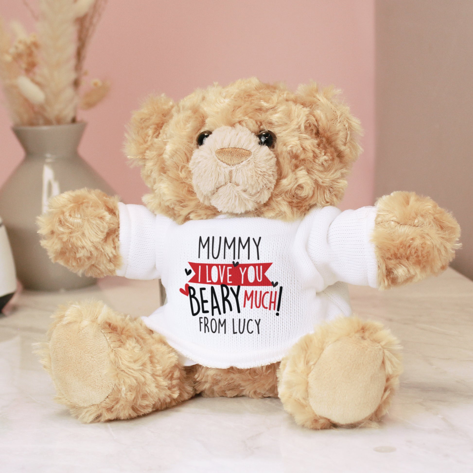 Teddy bear wearing a shirt with a personalised message on a light pink background