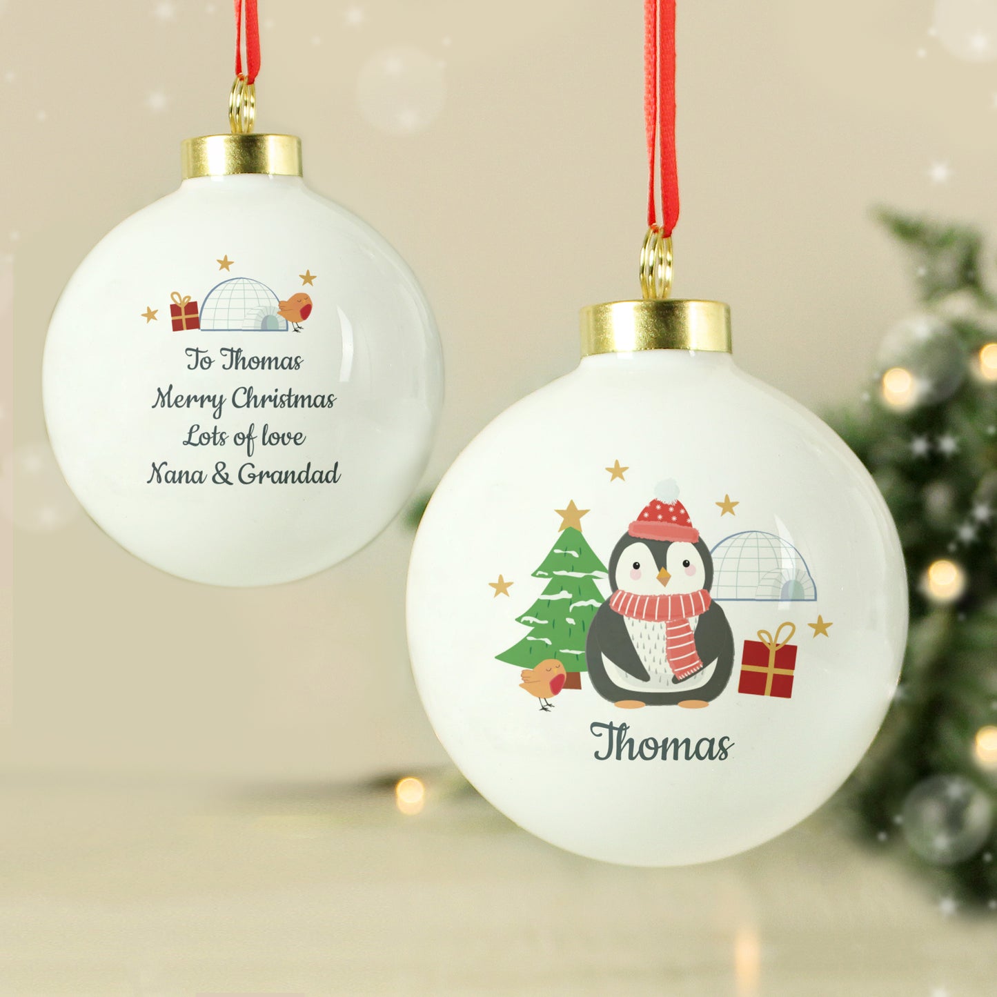 Two Christmas ornaments with a penguin design and personalised text, hanging against a festive background.