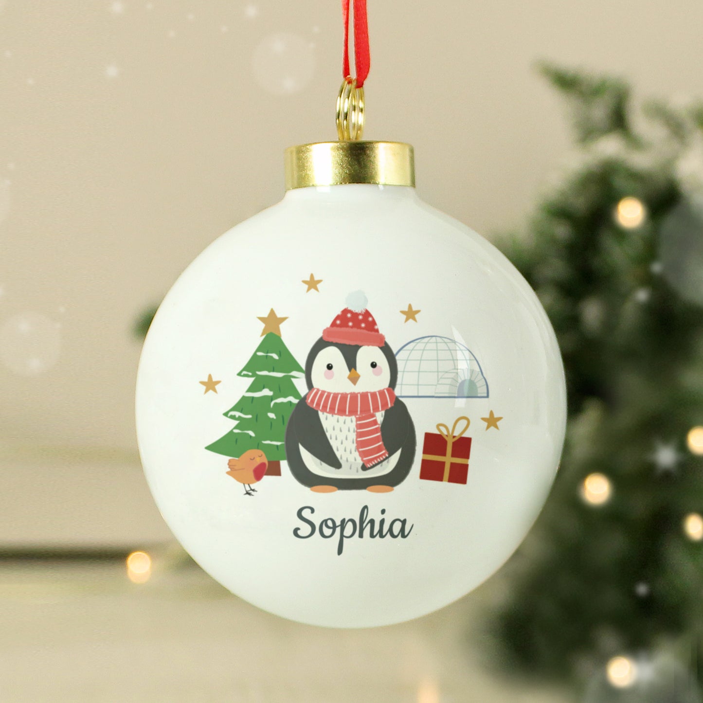 Christmas ornament with a penguin design and the name 'Sophia' on a blurred Christmas tree background.