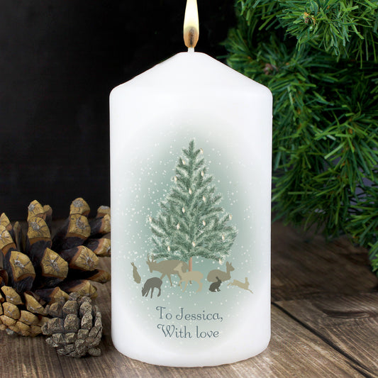 Personalised White candle with a Christmas design and text, surrounded by pinecones and a tree.