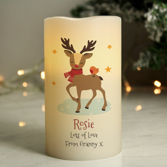 Decorative candle with a reindeer design and personalised text, set against a softly blurred background with lights.