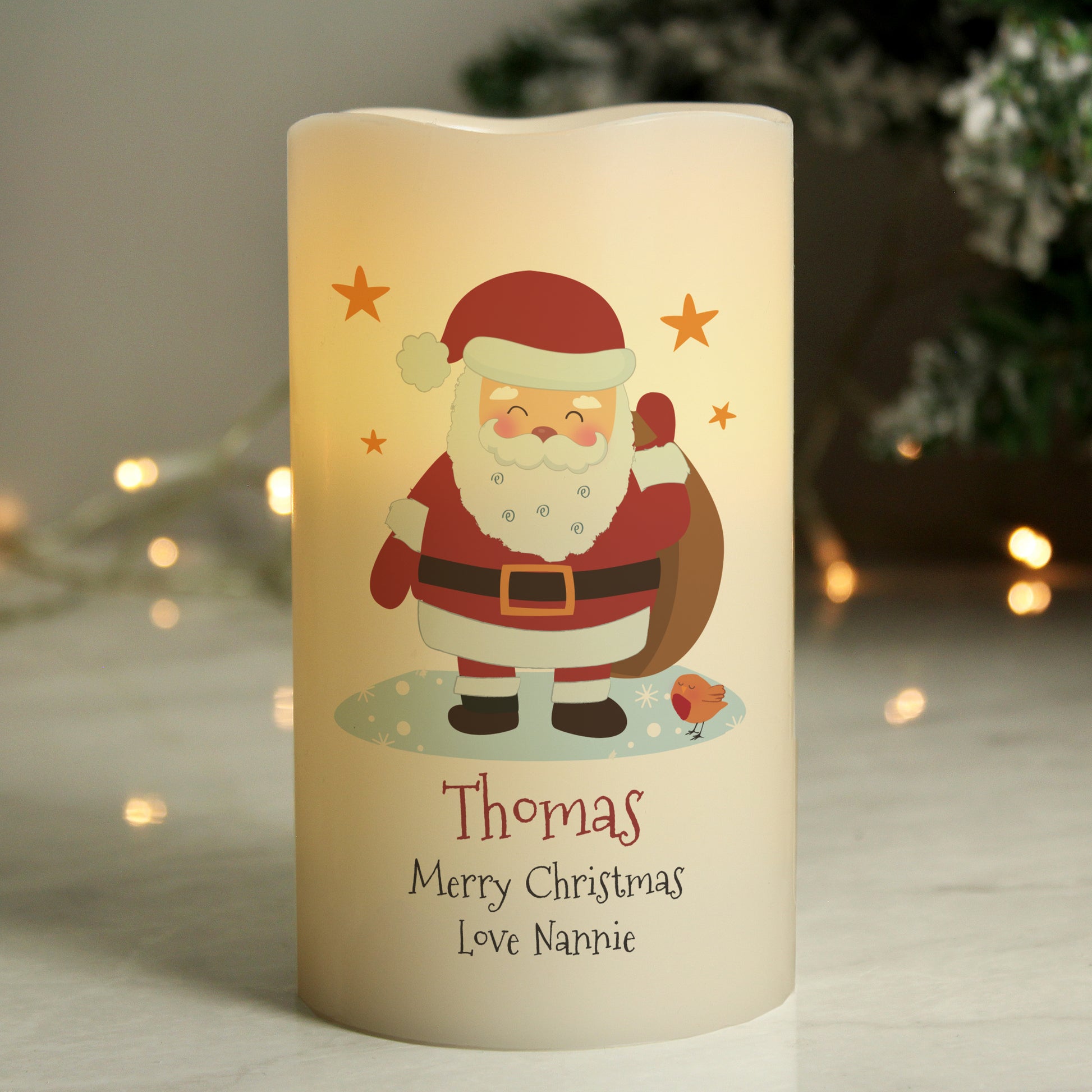 Decorative candle with Santa Claus illustration and personalised text, set against a blurred festive background.