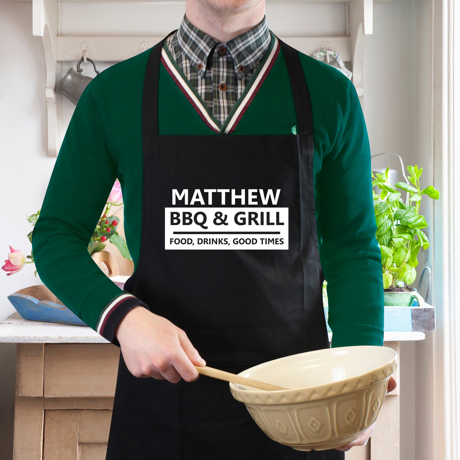 Person wearing a personalised black apron with 'Matthew BBQ & Grill' text in a kitchen setting