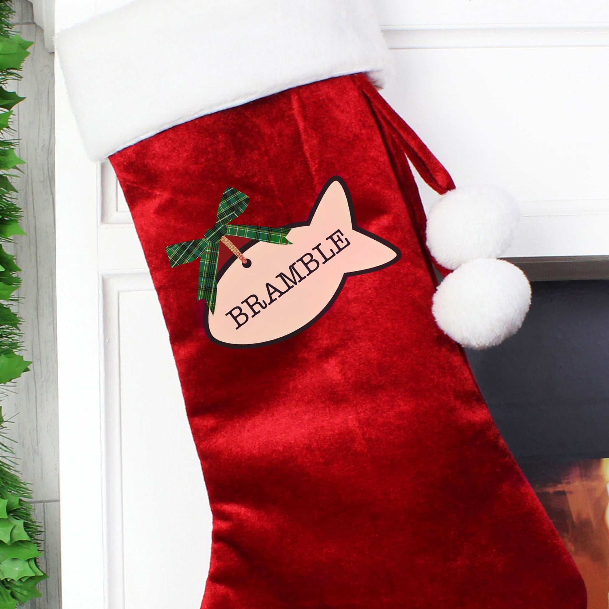 Red Christmas stocking with a tag and green bow, hanging on a fireplace.