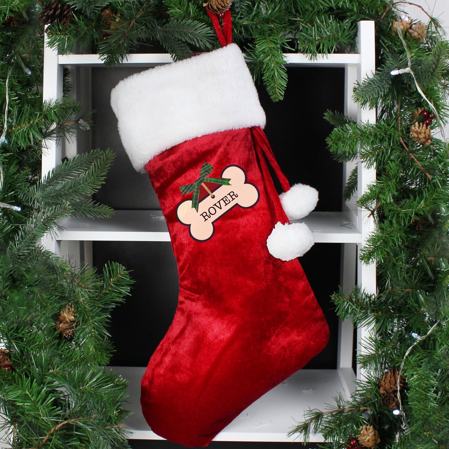 Red Christmas stocking with white trim and a bone design, hanging among greenery.
