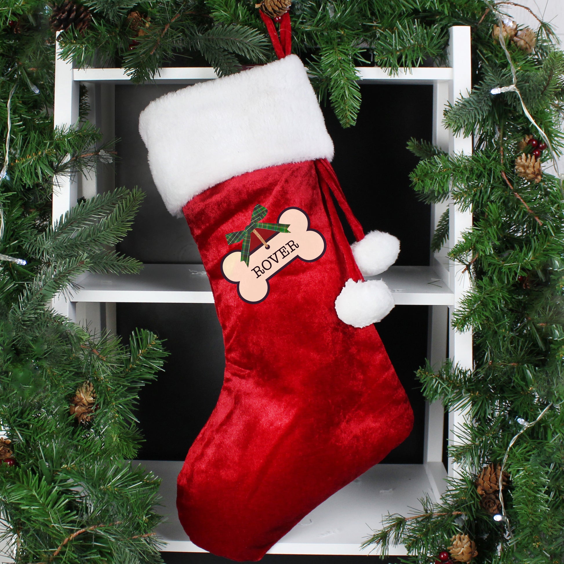 Red Christmas stocking with white trim and a bone design, hanging among greenery.