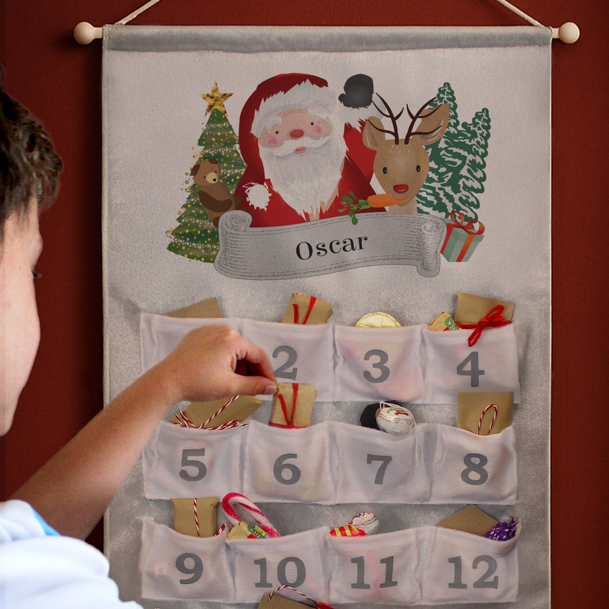 Child interacting with a Personalised Santa-themed advent calendar on a red wall.