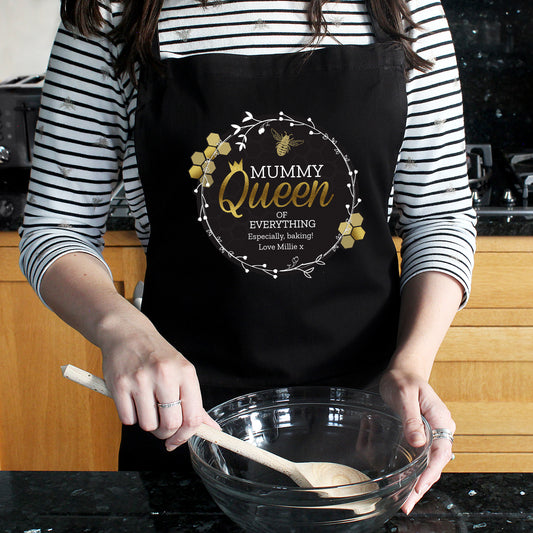 Person wearing a personalised black apron with 'Mummy Queen of Everything' text in a kitchen.