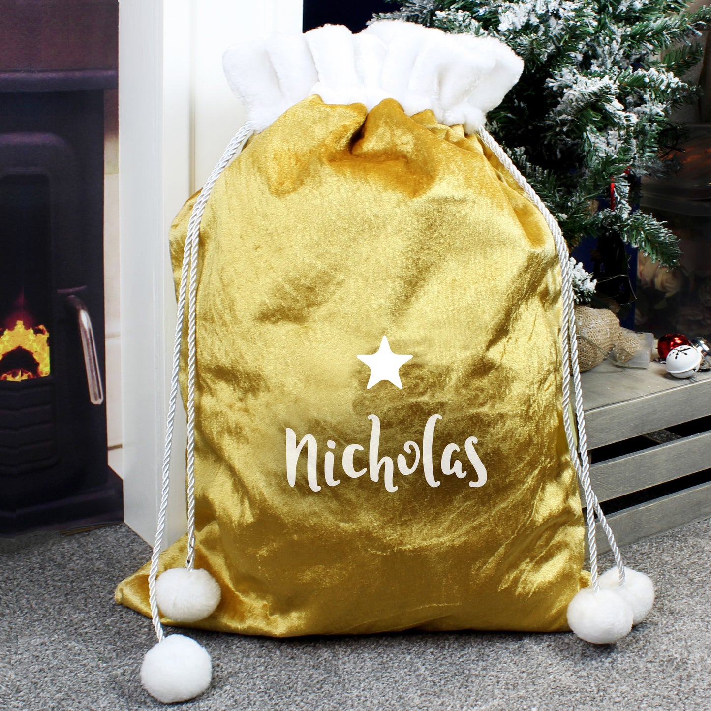 Gold drawstring bag with 'Nicholas' and a star, placed in front of a fireplace and Christmas tree.