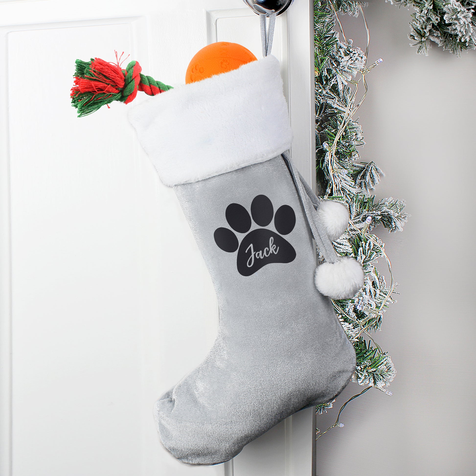 Gray Christmas stocking with a paw print and 'Jack' text, hanging on a white door with festive decorations.