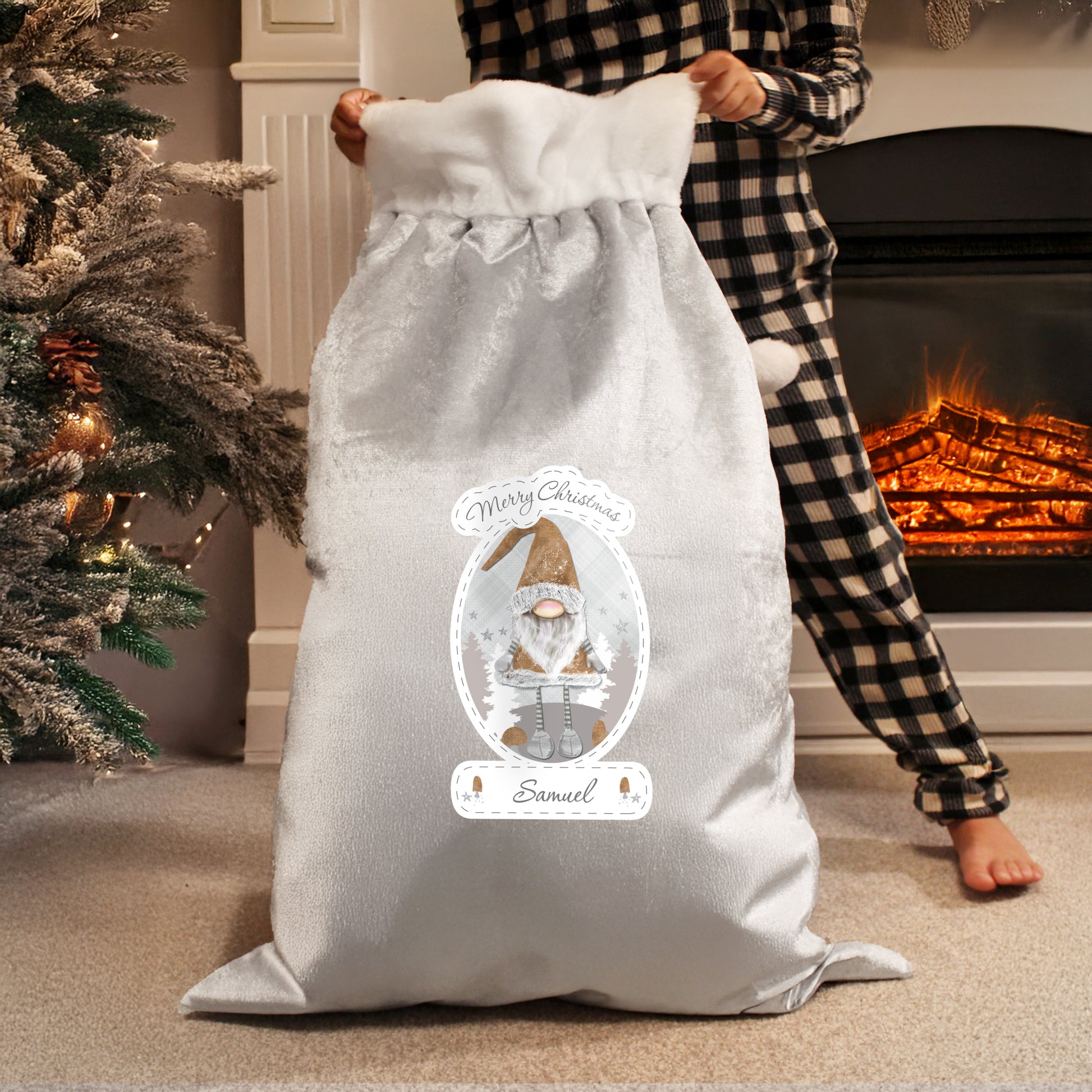 Person holding a grey Christmas sack with a personalised design in front of a fireplace.