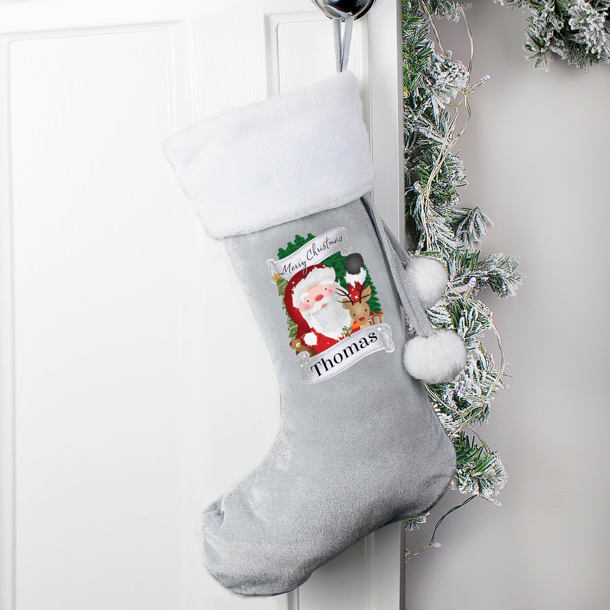 Grey Christmas stocking with Santa Claus design and 'Thomas' name tag, hanging on a white door with greenery.